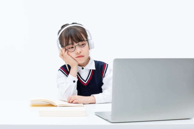 摄图网_501696025_小女孩坐在桌子前对着笔记本电脑发愁(非企业商用)